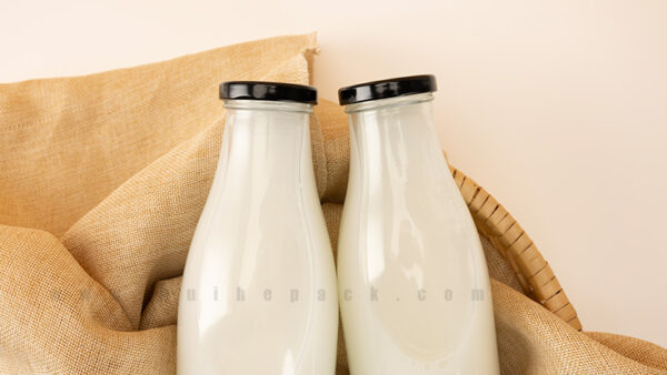 Two glass milk bottles filled with milk and closed with black caps